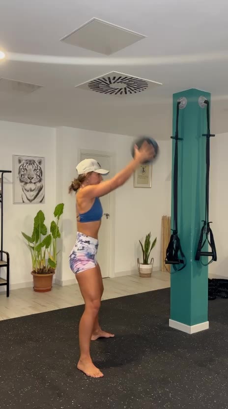 Verónica con un balón medicinal por encima de la cabeza junto a la columna verde del estudio